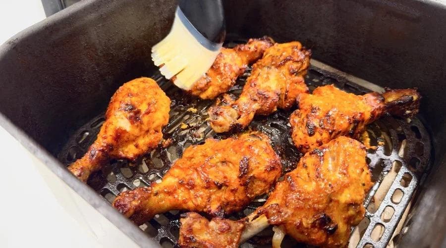 Tandoori chicken pieces in air fryer basket being brushed with melted butter during cooking.