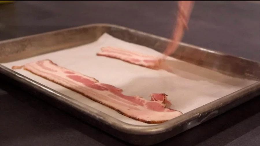 Strips of cooked bacon arranged on parchment paper in a baking sheet.