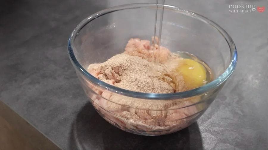 Ground chicken mixture with egg and cornstarch in a glass bowl, ready to be mixed together for nuggets.
