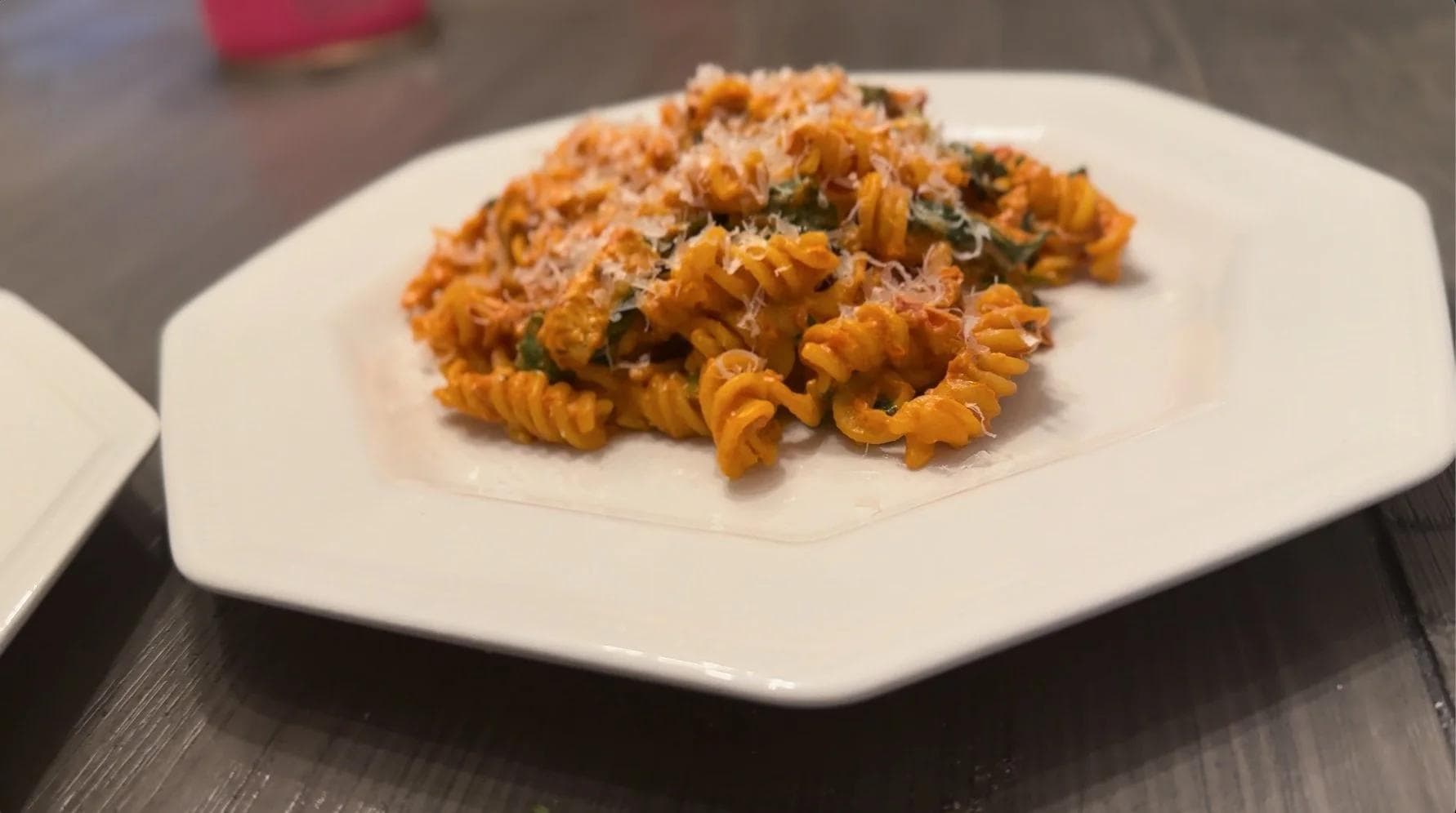 Gluten-free corn pasta with creamy tomato sauce, topped with grated cheese and herbs on a white plate.