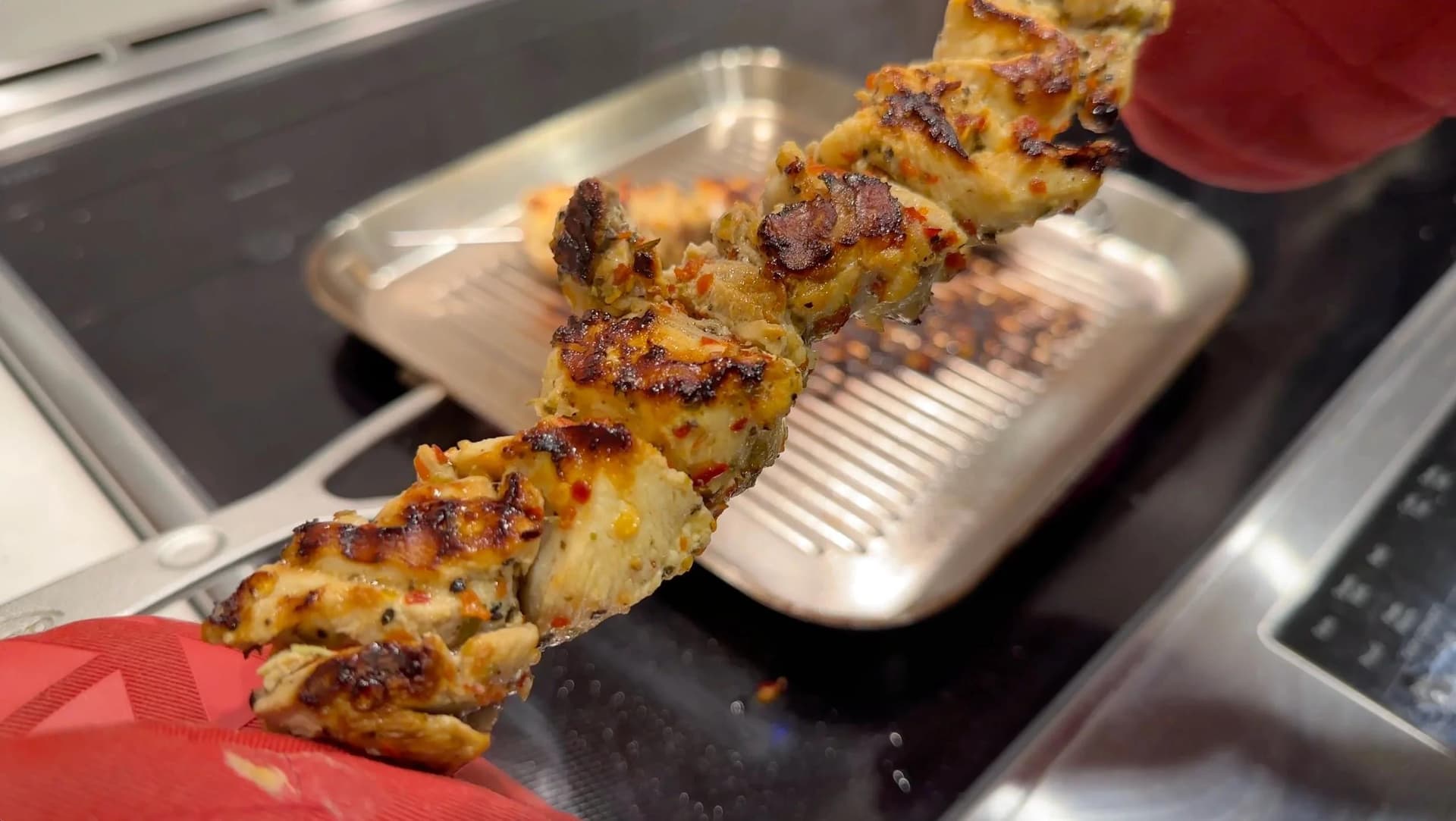 Grilled chicken souvlaki skewers with charred, golden-brown coating on a white plate in a grill pan.