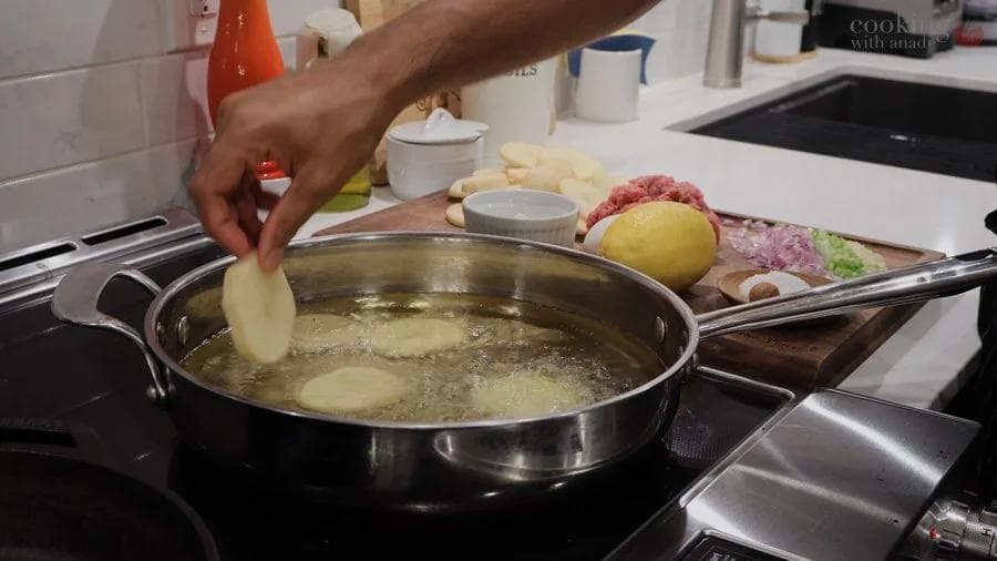 Hand dropping sliced potato into boiling water in a large pot on stovetop.