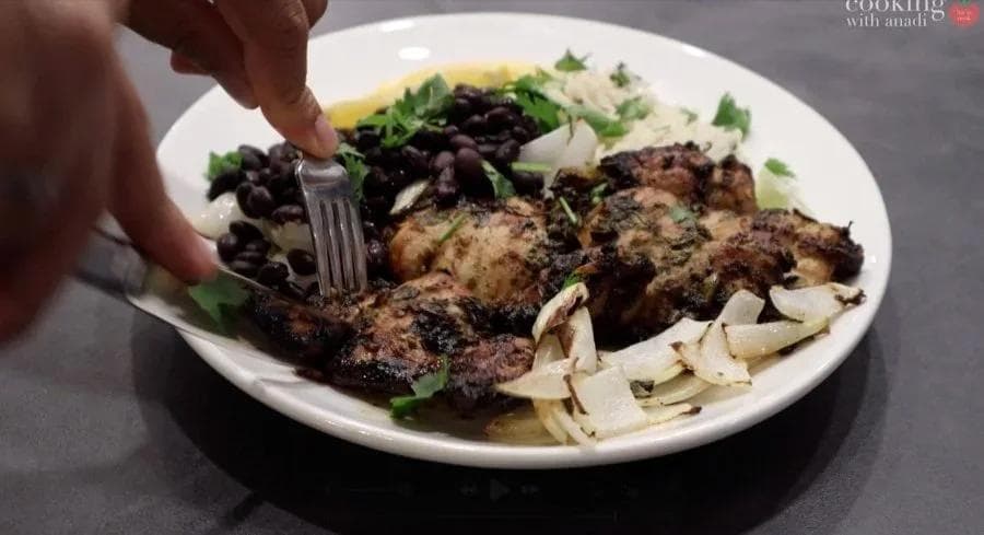 Plated Cuban mojo chicken with black beans, yellow rice, and sliced onions, fork cutting into the meat.