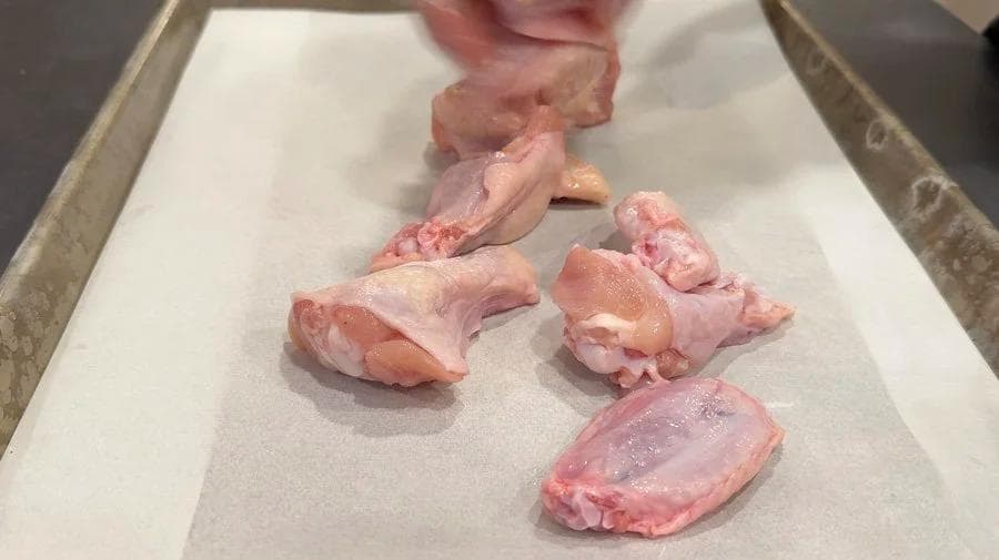 Raw chicken wings patted dry on parchment paper in a baking tray, ready for seasoning.