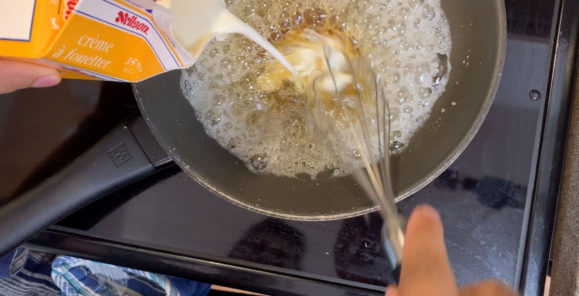 Pouring Wilton creme liqueur into bubbling caramel sauce in a saucepan on the stovetop.