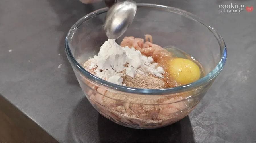 Ground chicken mixture with egg and cornstarch in a glass bowl being mixed with a spoon