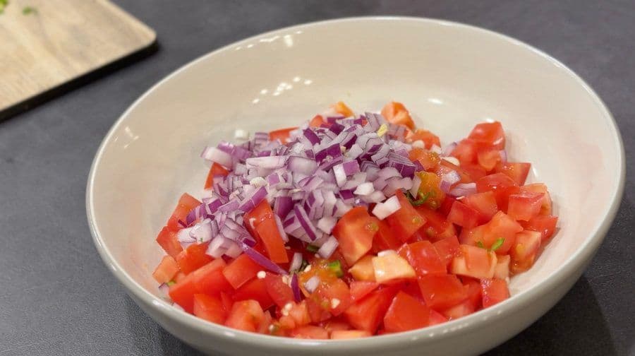 Diced red tomatoes and chopped red onions in a white bowl for pico de gallo preparation.