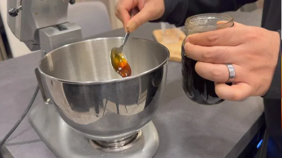 Pouring gingerbread sauce into a stand mixer bowl while holding a measuring cup.