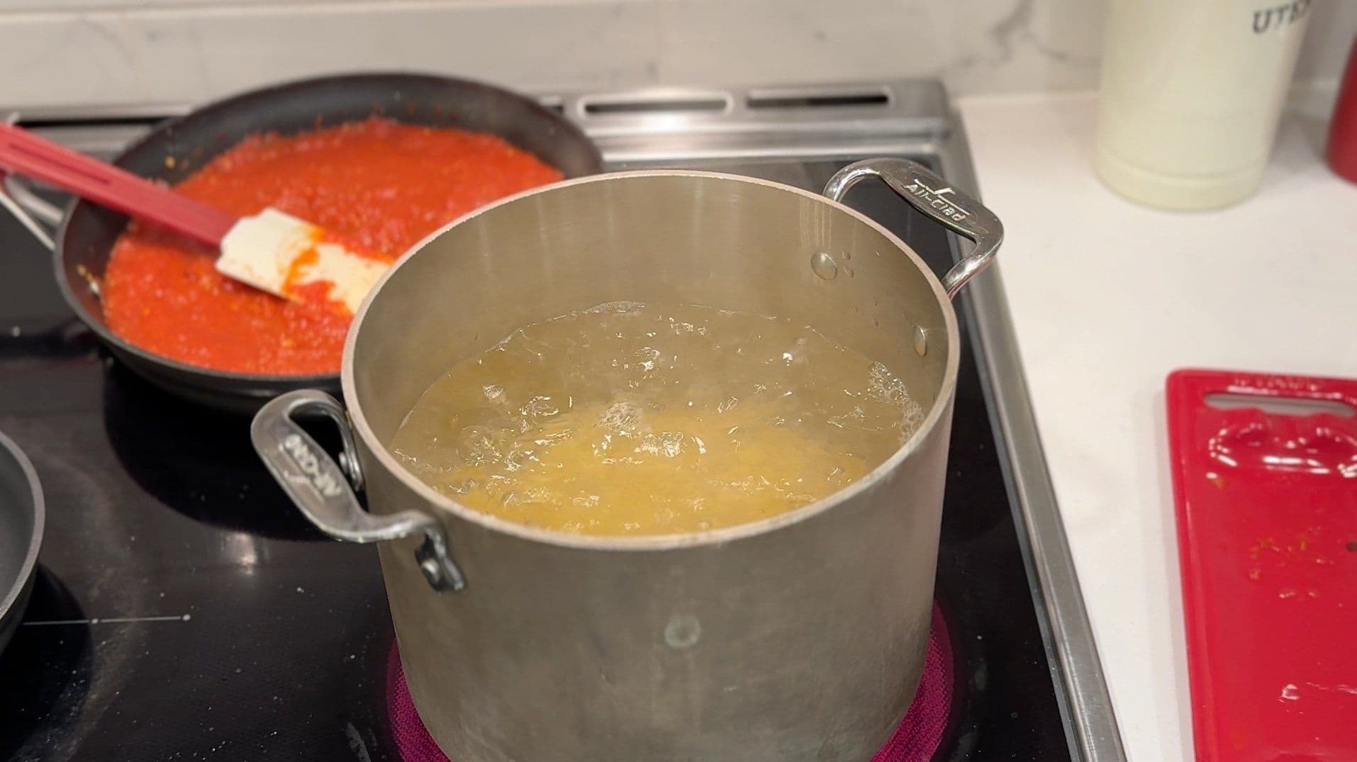 Pot of boiling water for pasta with pan of red marinara sauce cooking on stovetop.