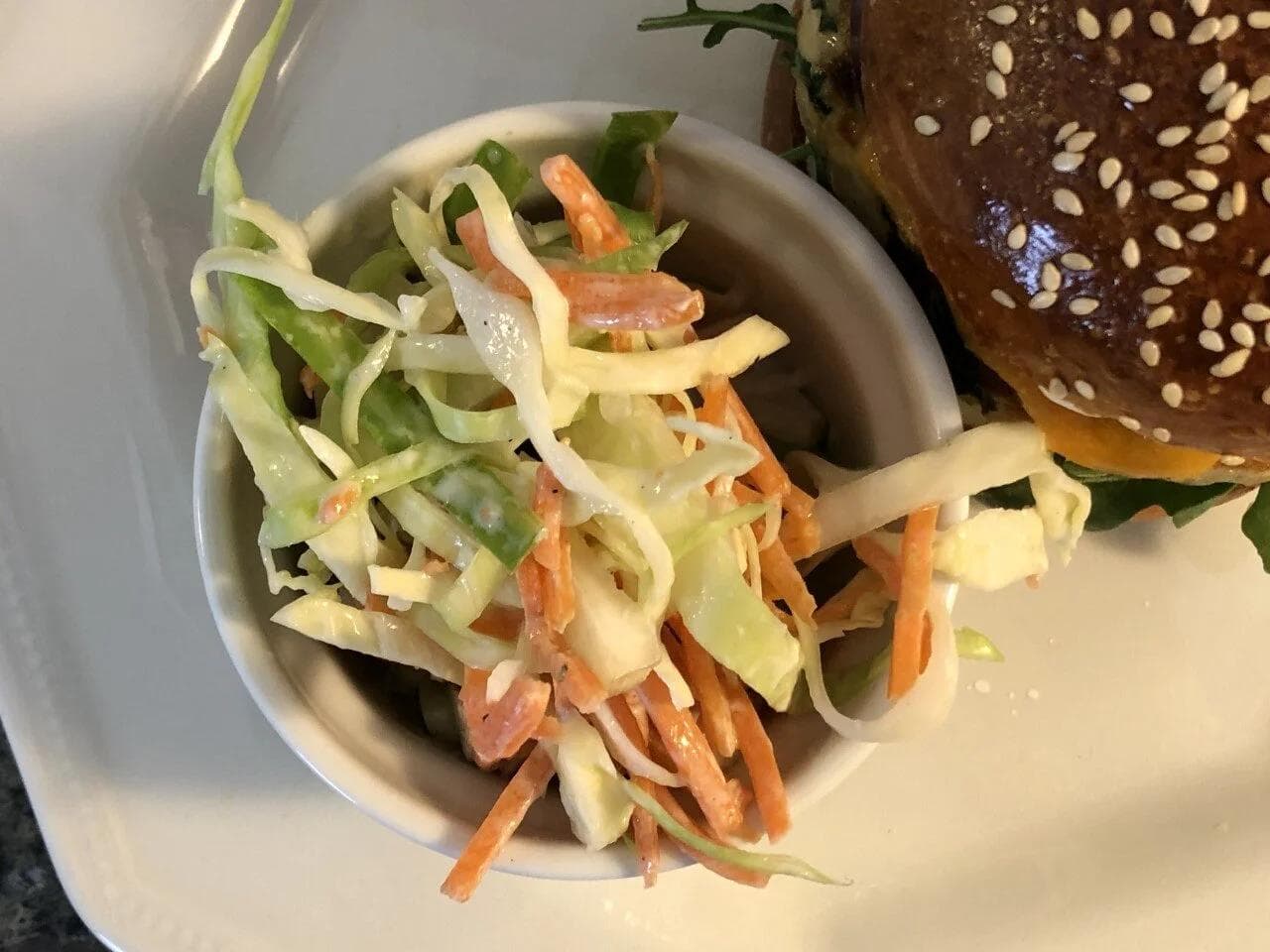 Creamy coleslaw with shredded cabbage, carrots, and green vegetables tossed together in a white bowl.