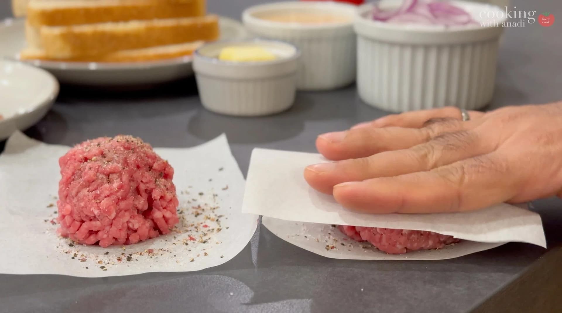 Hand pressing raw ground beef patties on parchment paper during smash burger preparation.