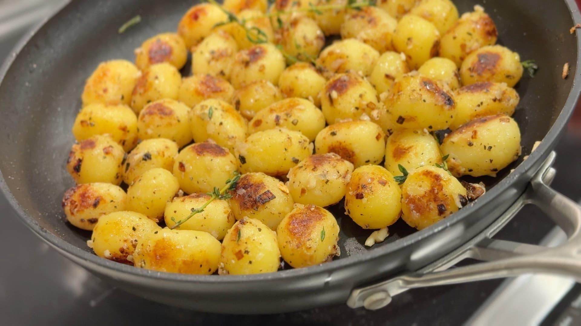 Golden-brown butter and garlic sautéed baby potatoes in a skillet, garnished with fresh herbs.