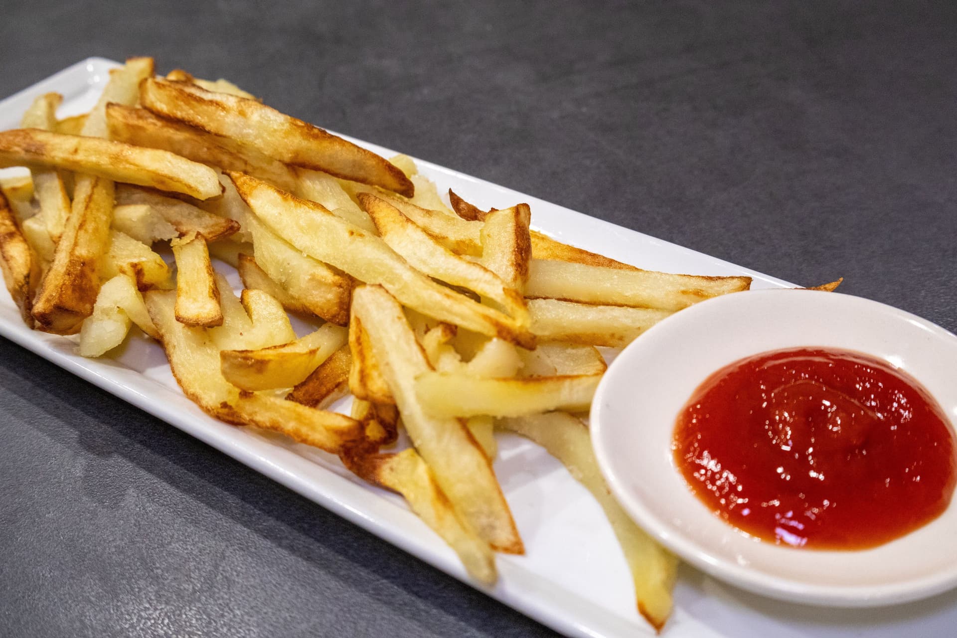 Crispy golden air fryer french fries on a white plate with a small bowl of ketchup for dipping.