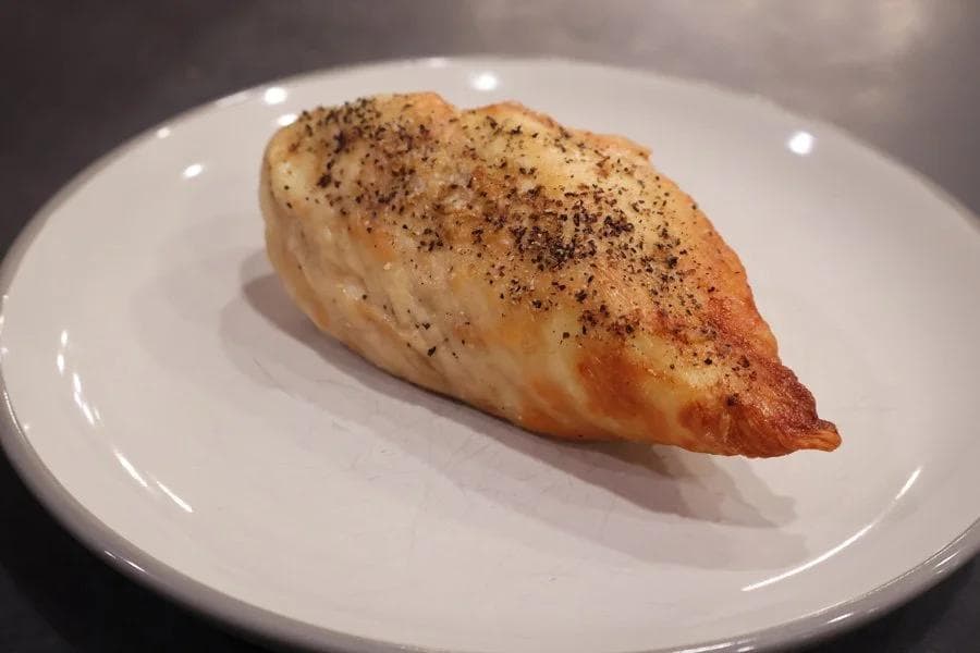 Seasoned air fryer chicken breast on a white plate, golden-brown and cooked through.
