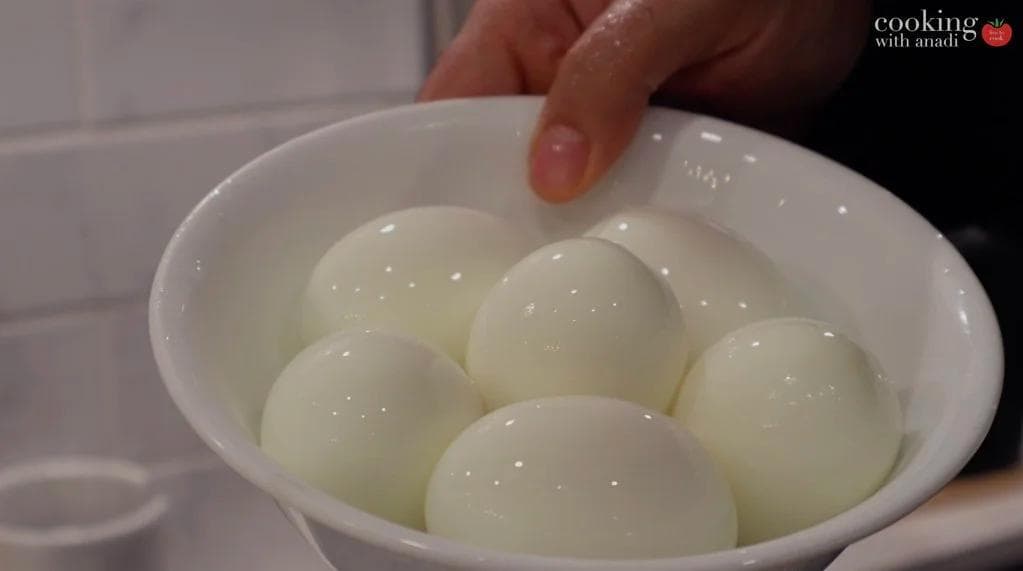 Peeled hard boiled eggs in a white bowl filled with water, cooling after boiling.