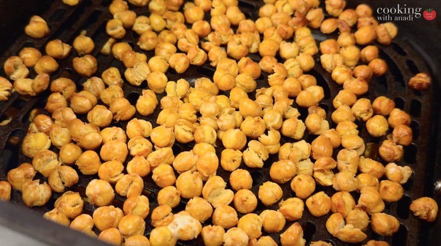 Crispy golden chickpeas spread in a single layer in an air fryer basket, evenly cooked and browned.