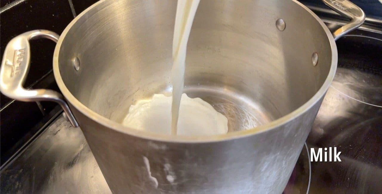 Milk being poured into a large stainless steel pot on the stovetop