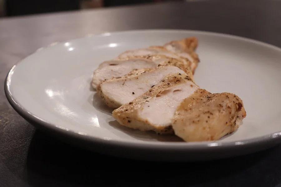 Sliced air fryer chicken breast with seasoned crust on a white plate, showing juicy interior.