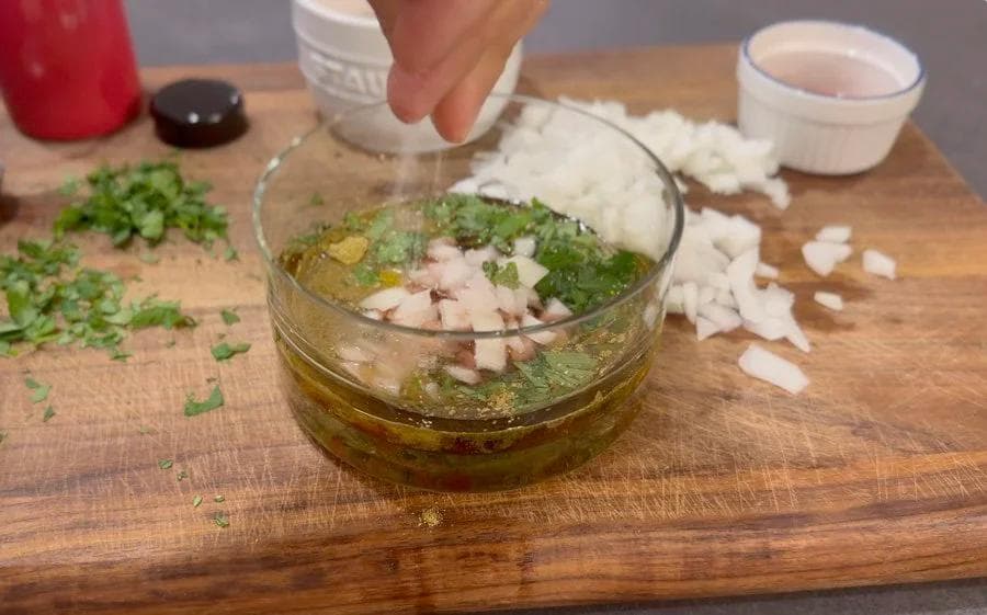 Chopped garlic and parsley being added to a bowl of chimichurri sauce with oil and vinegar.