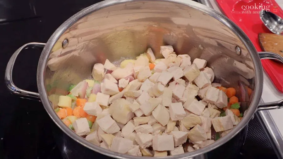 Diced chicken and cubed potatoes mixed with carrots and onions in a large pot during preparation.