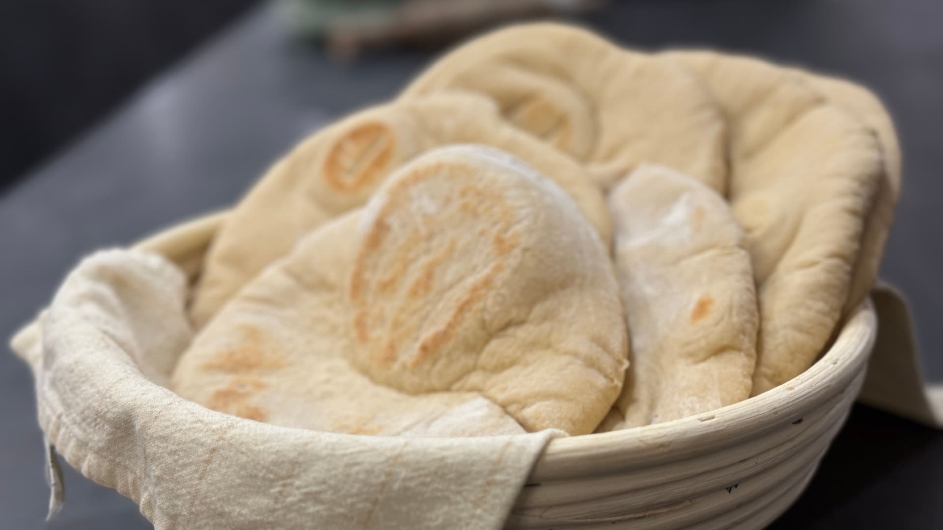 Unbaked Lebanese pita dough resting in a floured proofing basket, showing the characteristic oval shape and surface texture.