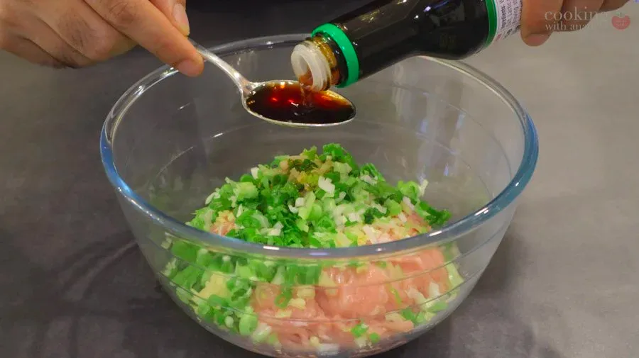 Dark soy sauce being poured from a bottle onto a bowl of ground chicken mixed with green onions and other ingredients.