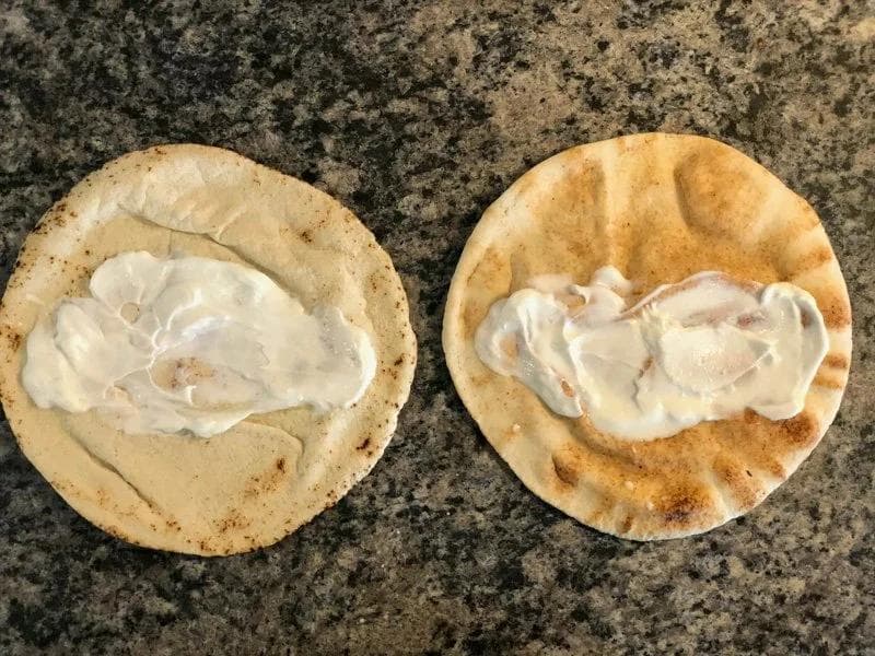 Two warm pita breads topped with dollops of Greek yogurt on a granite countertop.