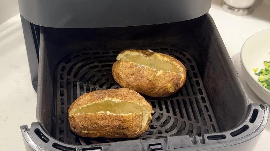 Two crispy potato shells with golden-brown skin in an air fryer basket after crisping at 390°F.