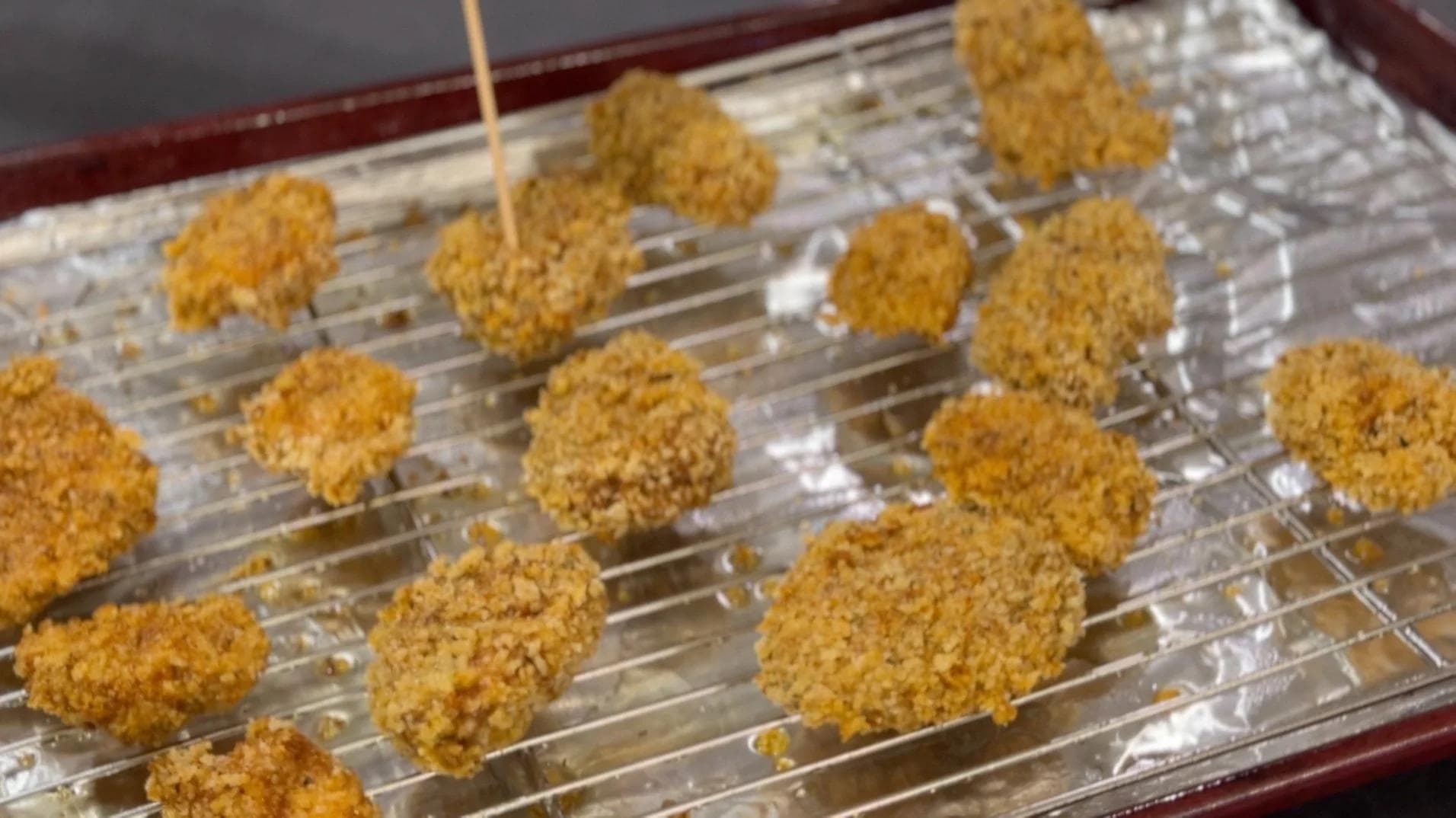 Golden panko-breaded chicken nuggets arranged on a wire rack lined with foil, ready for baking.