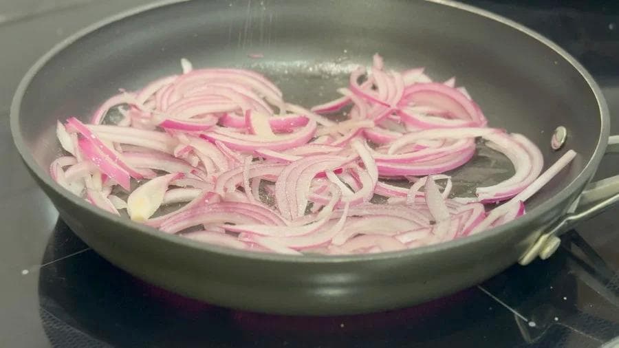 Sliced red and white onions sautéing in a pan with butter on medium heat.