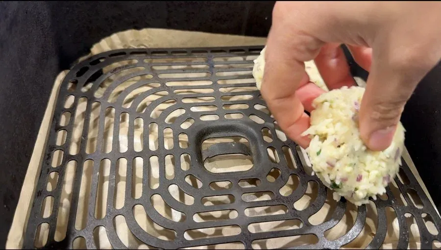 Hand placing a flattened rice fritter onto an air fryer basket tray before cooking.