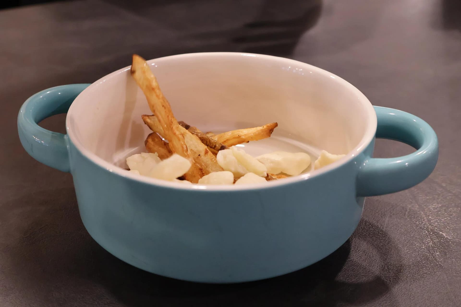 Light blue bowl with crispy fries, white cheese curds, and creamy sauce layered together.