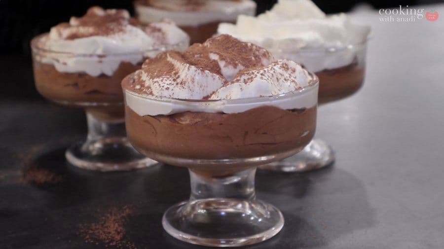 Chocolate mousse in glass dessert cups topped with whipped cream and cocoa powder dusting.