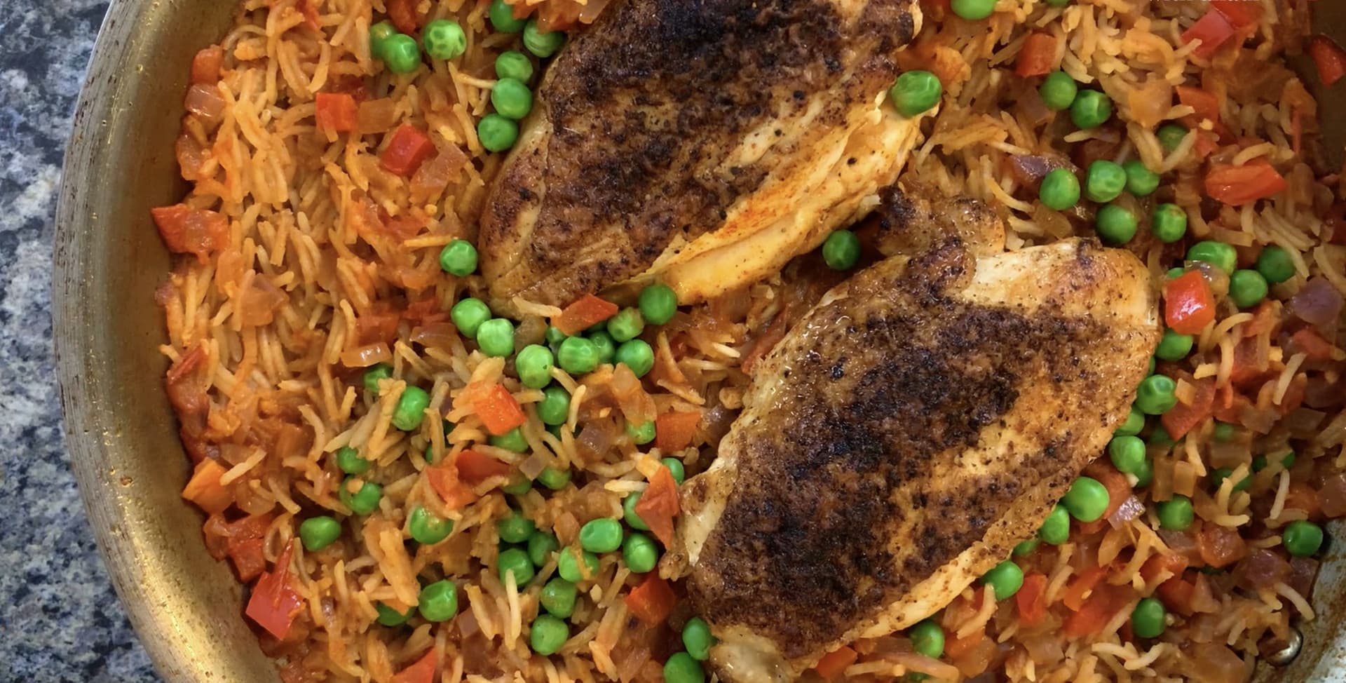 Two seasoned chicken breasts nestled in spicy rice with peas and diced tomatoes in a one-pot skillet.