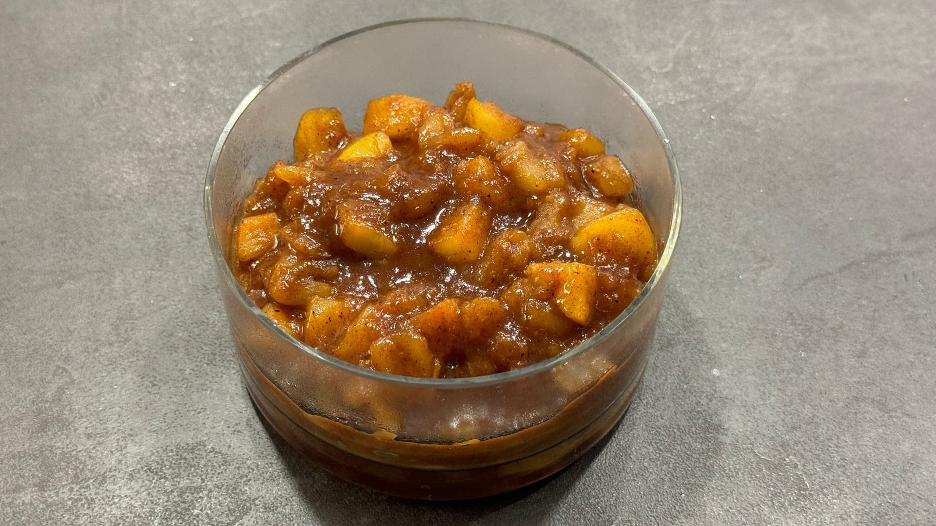 Homemade apple pie filling with chunks of cooked apples in a caramel-brown sauce in a clear glass bowl.