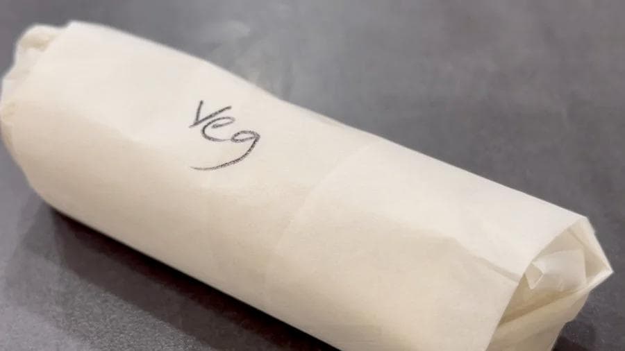 Breakfast burrito wrapped in parchment paper labeled "veg 9" on gray surface.