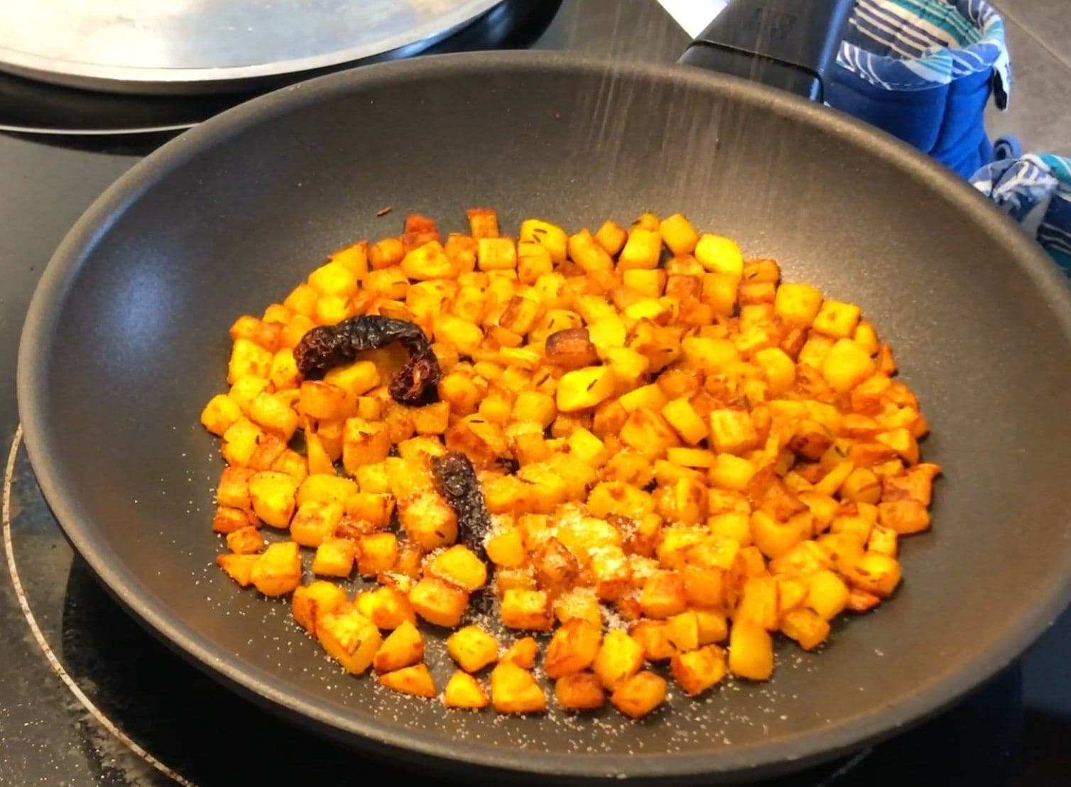 Golden diced potatoes sautéed with turmeric and dried chili in a dark nonstick skillet, nearly finished cooking.