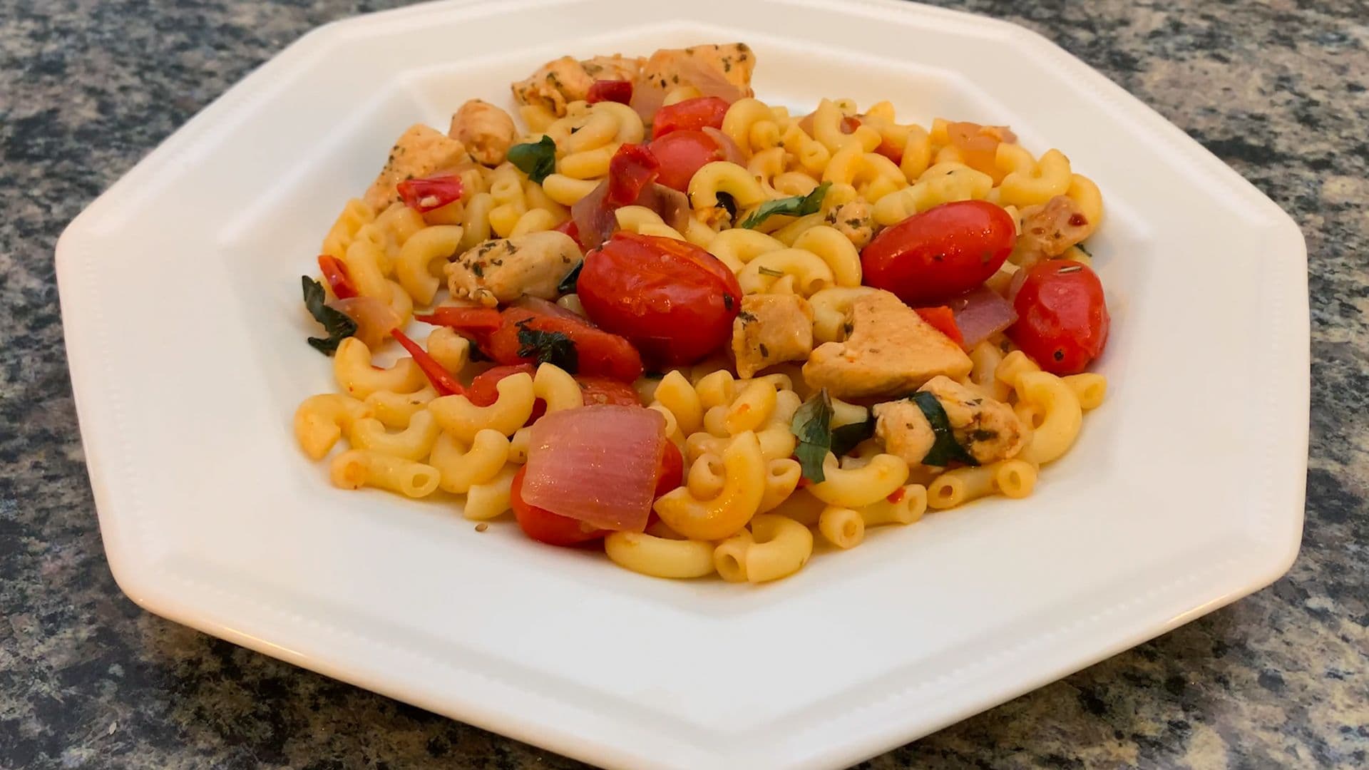 Plated chicken veggie pasta with elbow noodles, diced red peppers, chicken pieces, and fresh basil on white dish.