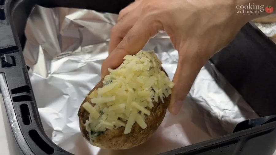 Hand holding a twice-baked potato topped with melted golden cheddar cheese before air frying.