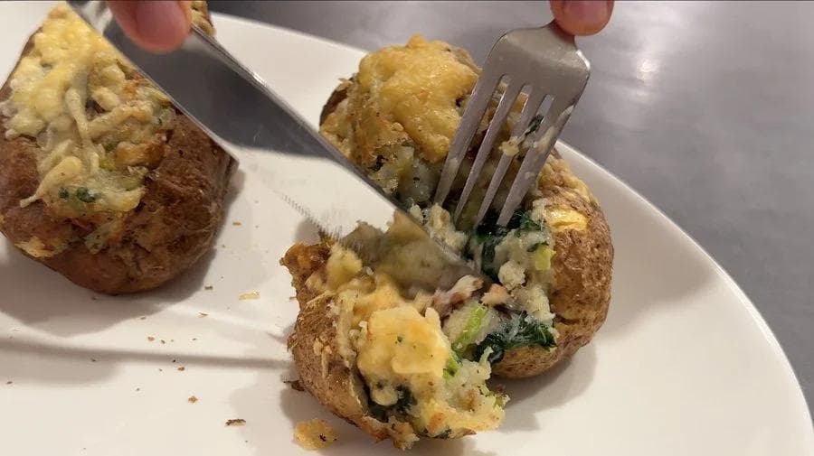Air fryer twice baked potatoes with Irish colcannon filling being cut open with a fork on a white plate.