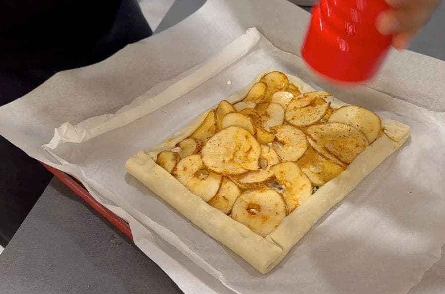 Baked puff pastry tart with sliced golden potatoes on ricotta filling and folded pastry edges in a white box.