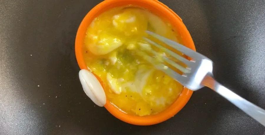 Scrambled eggs cooking in an orange silicone ring on a skillet, being stirred with a fork.