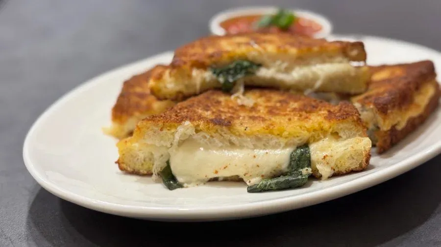 Golden-brown mozzarella in carrozza sandwich with melted cheese and basil visible between toasted bread slices on a white plate.