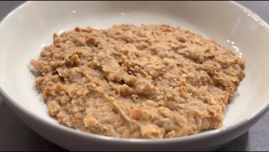Creamy mashed refried beans in a white bowl, showing a thick, chunky texture ready to serve.