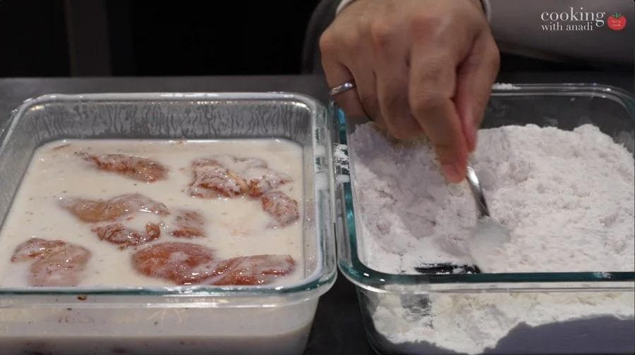 Chicken pieces being coated in seasoned flour mixture for breading, with buttermilk marinade on left and flour mix on right.