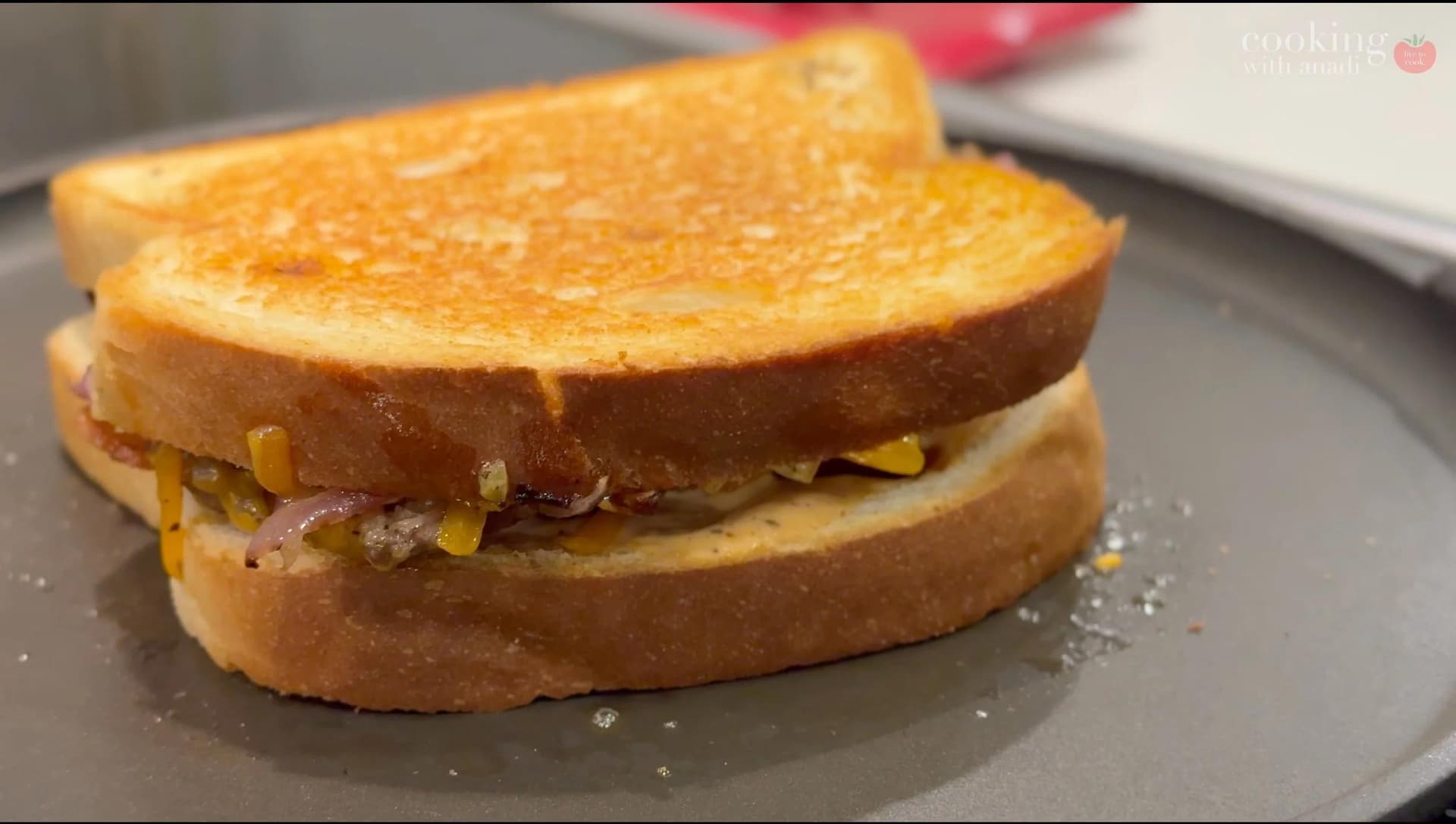 Golden brown smash burger patty melt with caramelized onions on toasted bread on a gray plate.
