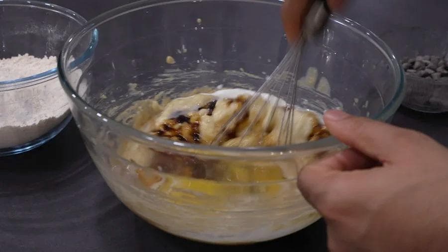 Whisking mashed bananas with butter and sugar mixture in a glass bowl during banana bread preparation.