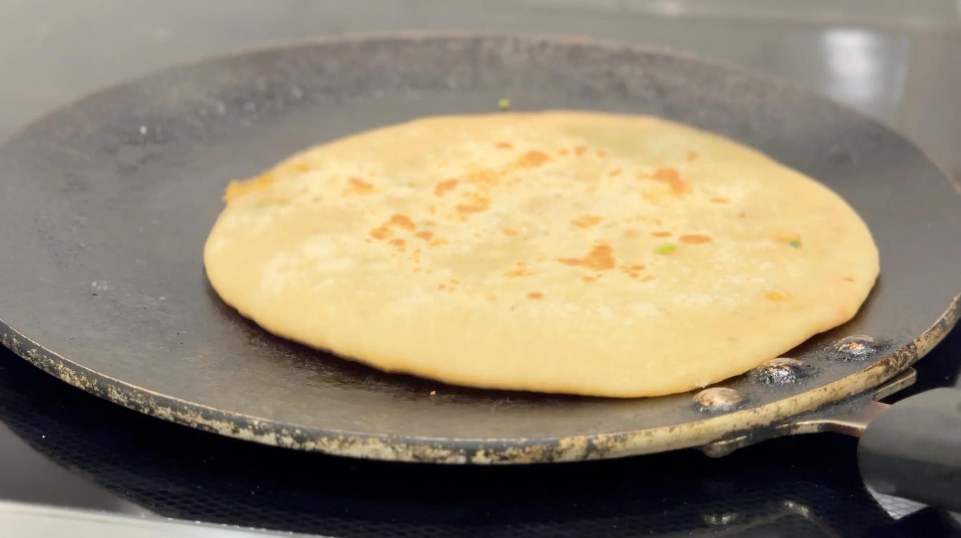 Gobi paratha cooking on a tawa with golden-brown spots on the surface.