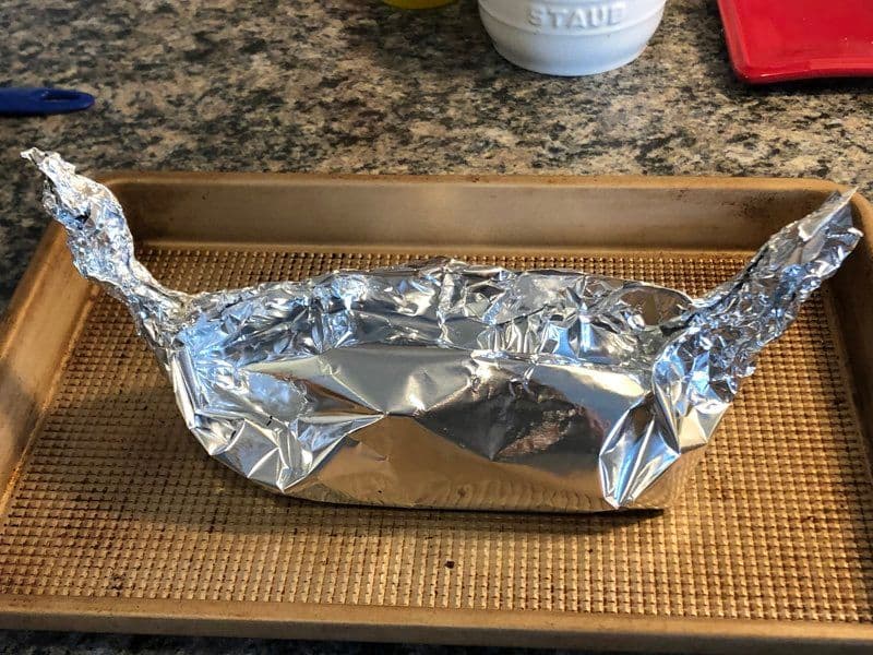 Salmon fillet wrapped in aluminum foil on a baking sheet lined with parchment paper, ready to bake.