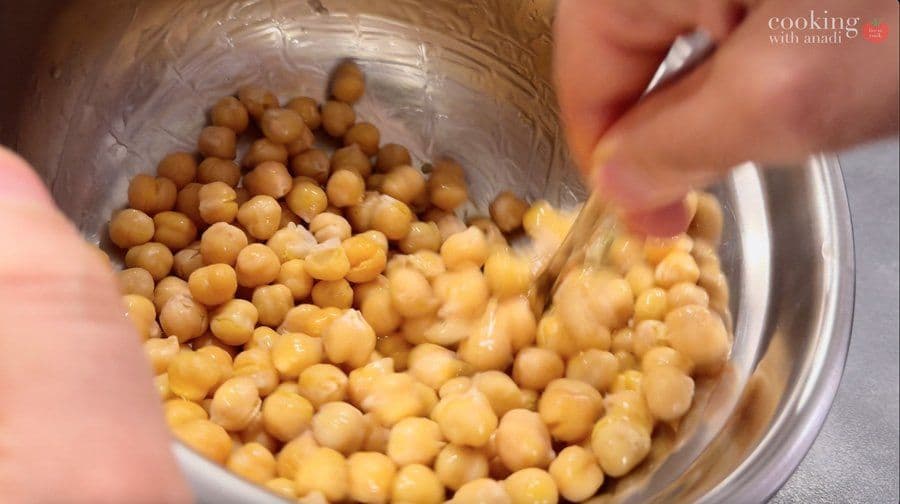 Chickpeas drizzled with olive oil being poured into an air fryer basket for cooking.
